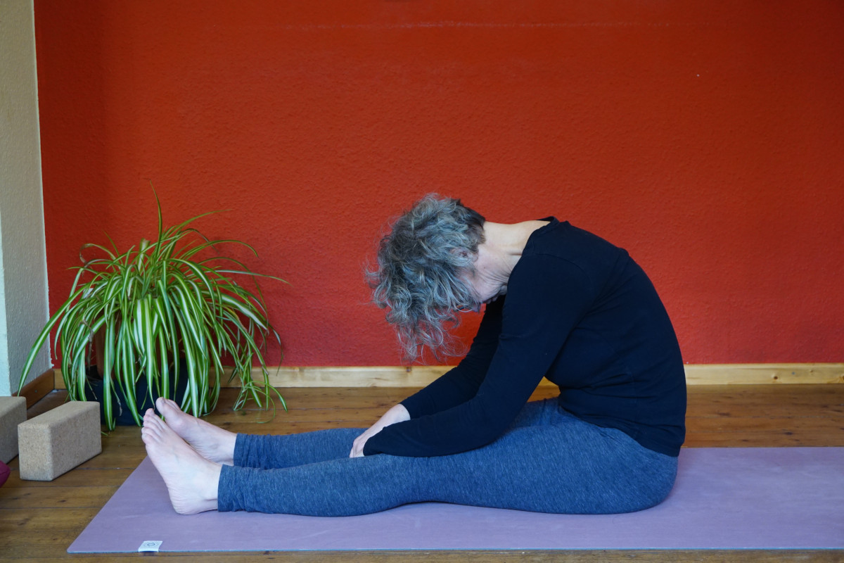 Susanne in der Yin Yoga Postion Raupe. Dabei sind die Beine auf dem Boden sitzend nach vorne gestreckt, der Oberkörper wird mit rundem Rücken nach vorne gebeugt.