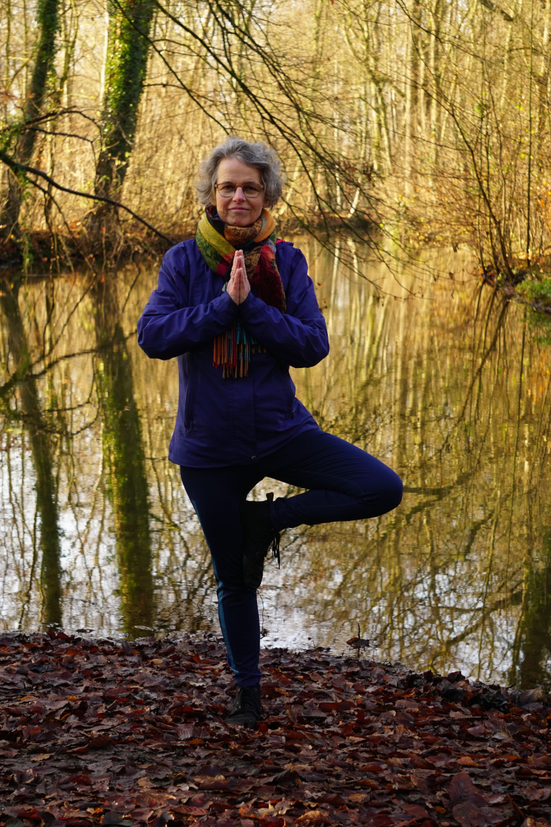 Susanne in der Yogaposition Baum. Im Stehen wird ein Bein angewinkelt und an der Fuß am Oberschenkel angelegt. Die Hände sind gefaltet.