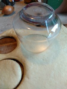 Das Foto zeigt einen ausgerollten Hefeteig. Mit einem Glas werden runde Formen ausgestochen.