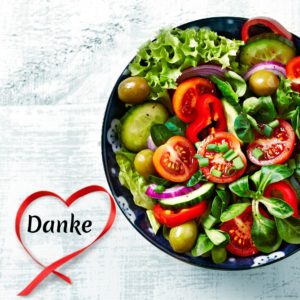 Das Foto zeigt eine Schüssel gemischten Salat. Mit Tomaten, Gurken, Oliven, Feldsalat, Blattsalat und Paprika. Unten ist eine rotes Band als Herz gelegt. In der Mitte des Herzens steht "Danke".