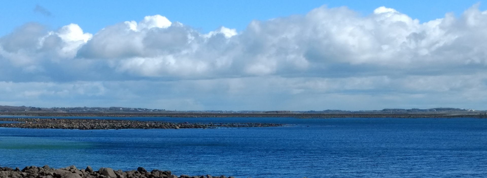 Foto der irischen See. Im Hintergrund ist eine Landzunge zu sehen. Die obere Hälfte des Bildes ist mit einem Wolkenhimmel bedeckt.